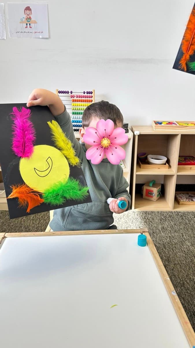 Child proudly showing art project with Arabic letter