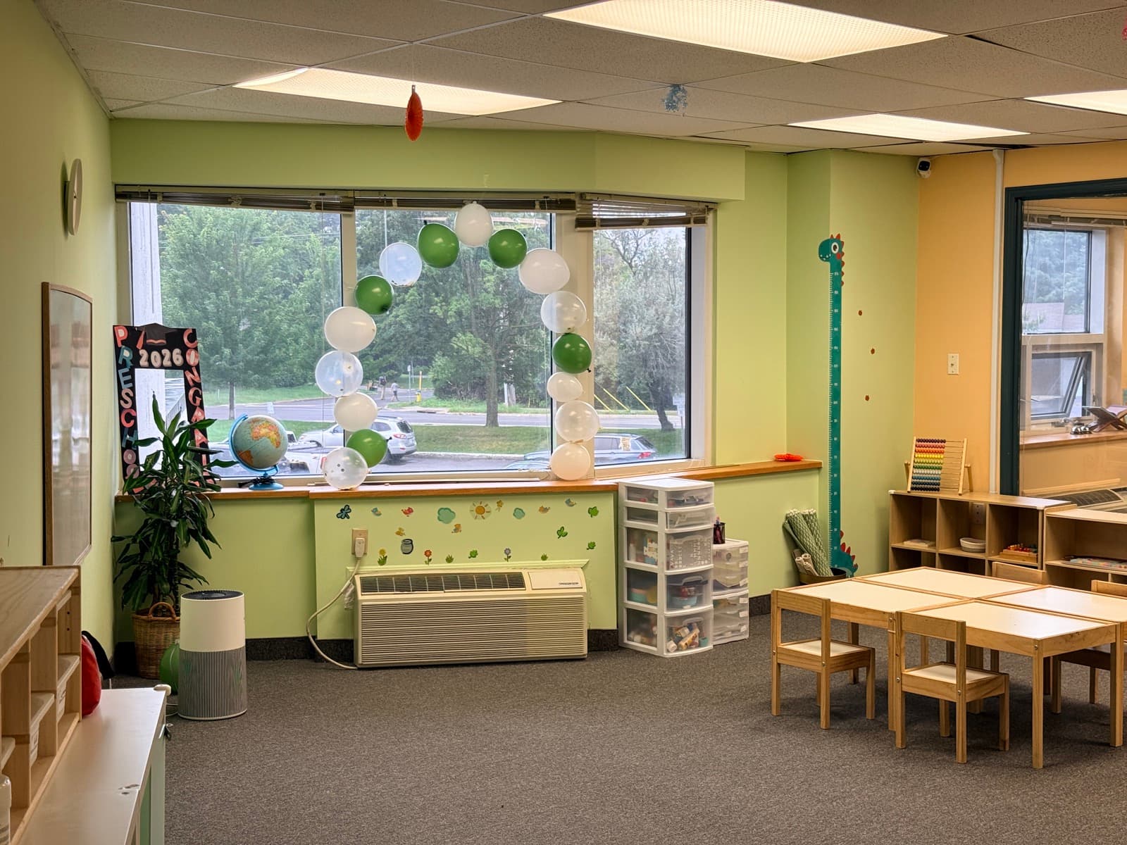 Bright classroom with a green and white balloon arch, child-sized tables, and Montessori shelves