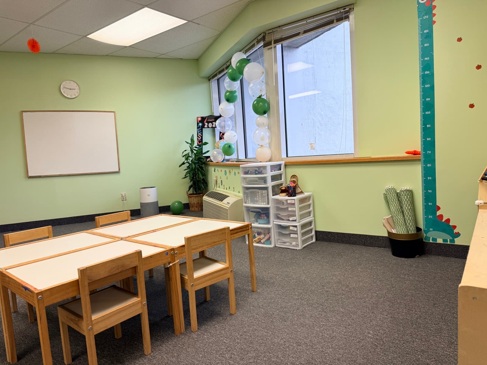 Classroom with child-sized tables, whiteboard, and a dinosaur growth chart on the wall