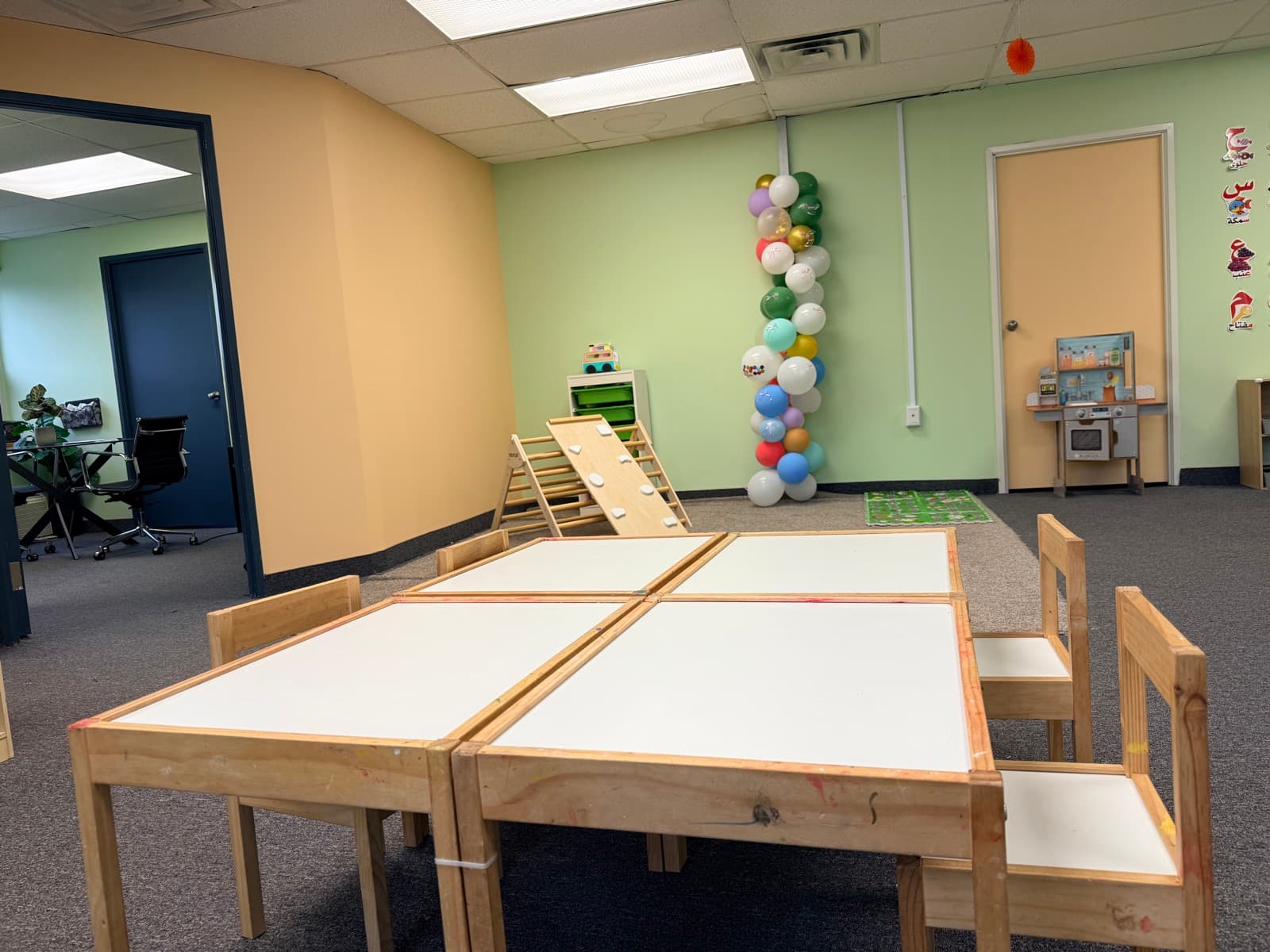 Open play area with activity tables, a climbing triangle with slide, and a play kitchen