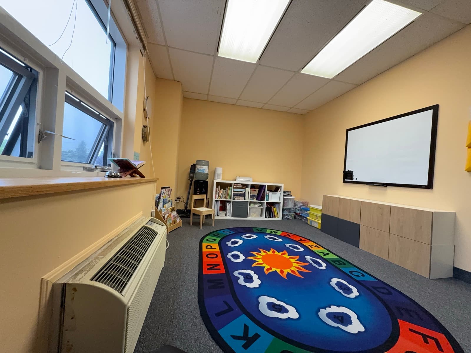 Circle-time room with alphabet rug, book shelf, and bright windows