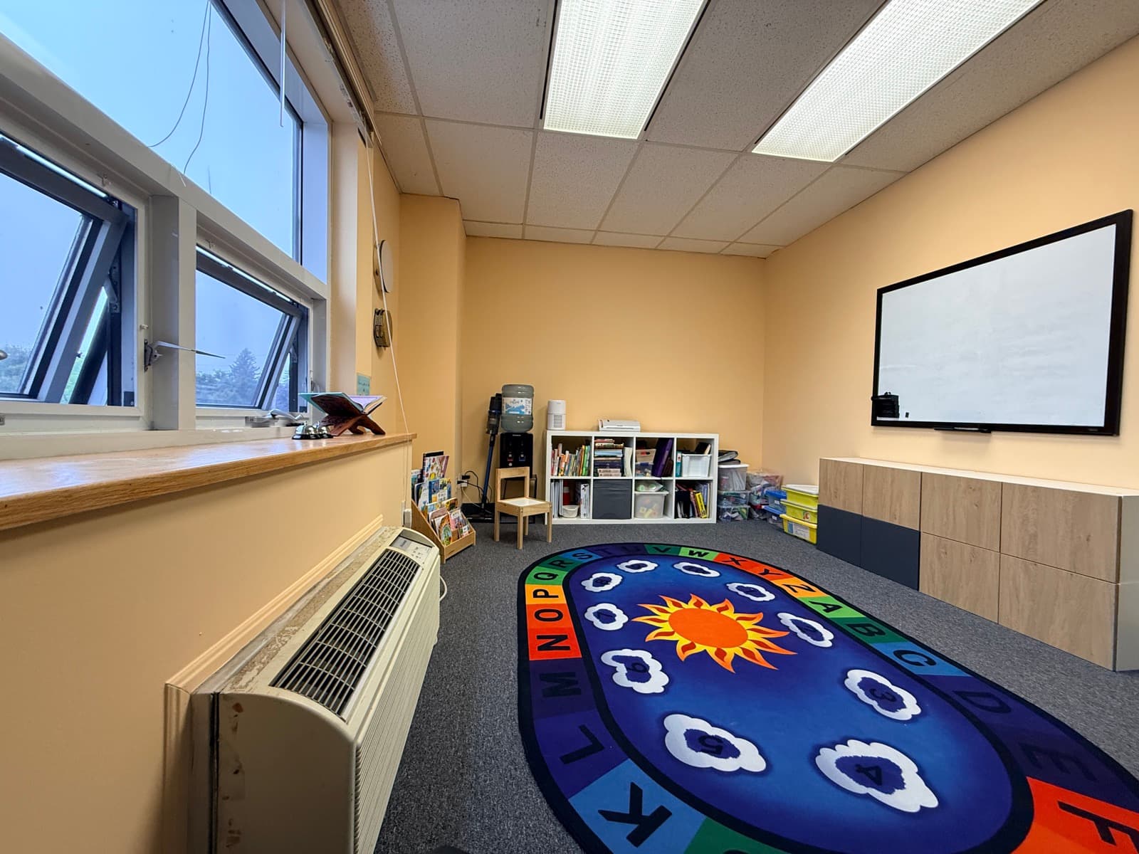 Cozy circle-time room with a colourful alphabet rug and wall-mounted whiteboard